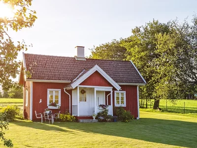 Kleines Bauernhaus steht auf grüner Wiese umgeben von Bäumen