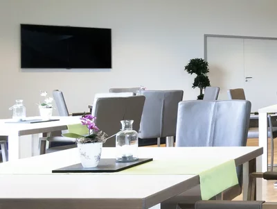 Seminarbewirtung Moderner Besprechungsraum mit grauen Stühlen, weißen Tischen und einer Theke im Hintergrund.
