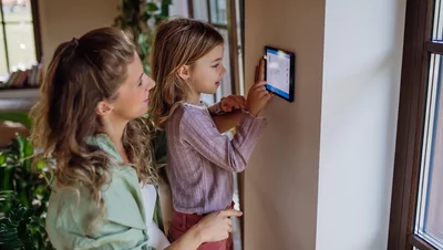 Welche Wärmepumpe ist die richtige für mein Zuhause? Mutter und Tochter bedienen ein Wand-Touchscreen-Display zur Regelung der Raumtemperatur