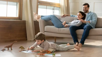 Glückliche Familie im Wohnzimmer: Eltern entspannen auf dem Sofa, während das Kind auf dem Boden spielt