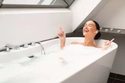 Eine Frau entspannt sich in einer Badewanne mit Schaum und hört dabei Musik