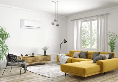 Wit wandapparaat van een airconditioning in een moderne woonkamer met een gele bank en houten dressoir.