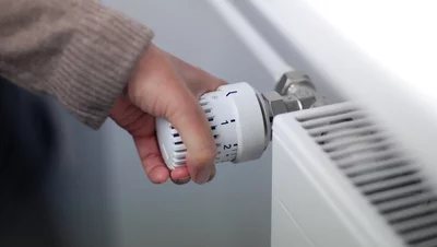 Sind Gasheizungen 2026 verboten? Hand dreht Thermostatventil an einem weißen Heizkörper zur Temperaturregelung