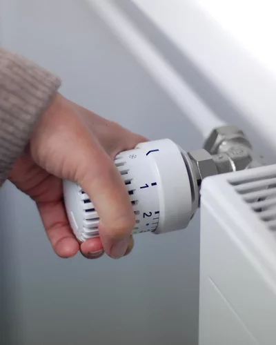 Sind Gasheizungen 2026 verboten? Hand dreht Thermostatventil an einem weißen Heizkörper zur Temperaturregelung