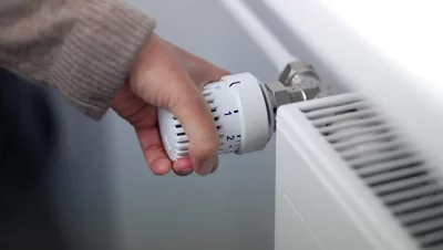 Sind Gasheizungen 2026 verboten? Hand dreht Thermostatventil an einem weißen Heizkörper zur Temperaturregelung