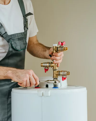 Handwerker montiert eine Armaturgruppe an einem weißen Warmwasserspeicher
