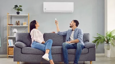 Ein Paar sitzt auf einem Sofa und bedient eine Remko Wandklimaanlage mit einer Fernbedienung
