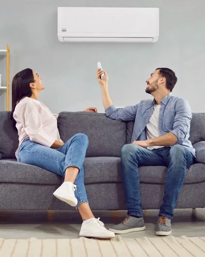 A couple sits on a sofa and operates a Remko wall-mounted air conditioner with a remote control.