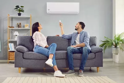 Die Luft-Luft-Wärmepumpe als Klimaanlage Ein Paar sitzt auf einem Sofa und bedient eine Remko Wandklimaanlage mit einer Fernbedienung