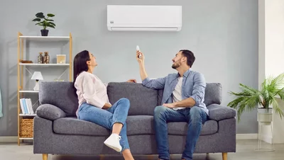Ein Paar sitzt auf einem Sofa und bedient eine Remko Wandklimaanlage mit einer Fernbedienung