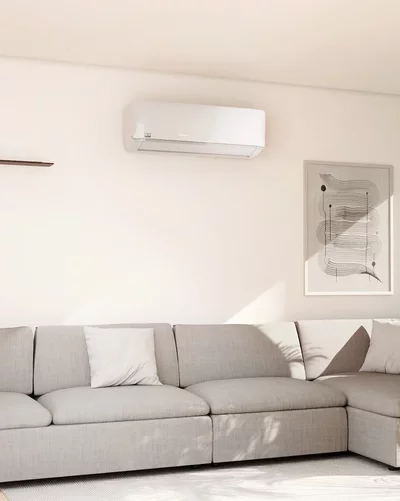 Helles Wohnzimmer mit grauem Ecksofa und einem weißen Remko Klimagerät an der Wand