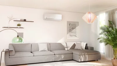 Helles Wohnzimmer mit grauem Ecksofa und einem weißen Remko Klimagerät an der Wand