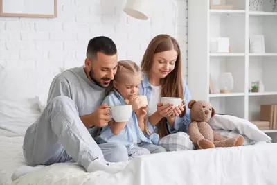 Familie im Pyjama trinkt auf dem Bett heiße Getränke