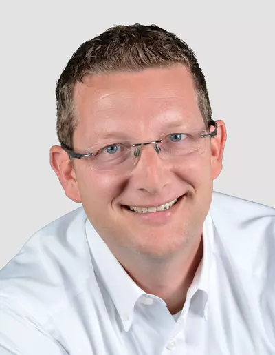 Nils Quentmeier Porträt eines lächelnden Mannes mit Brille und weißem Hemd vor neutralem Hintergrund