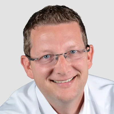 Nils Quentmeier Porträt eines lächelnden Mannes mit Brille und weißem Hemd vor neutralem Hintergrund