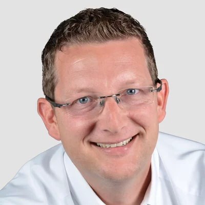 Nils Quentmeier Porträt eines lächelnden Mannes mit Brille und weißem Hemd vor neutralem Hintergrund