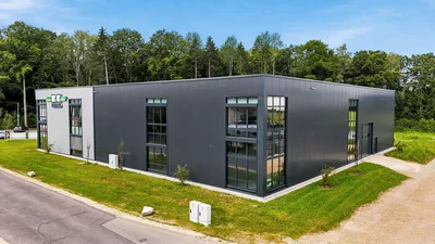 Schulungszentrum Süd<br>Illschwang Außenansicht des modernen Remko-Gebäudes mit dunkler Fassade und großen Fenstern, umgeben von Grünflächen und Bäumen.
