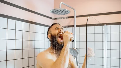 Mann mit Bart singt leidenschaftlich unter der Dusche und hält den Duschkopf wie ein Mikrofon