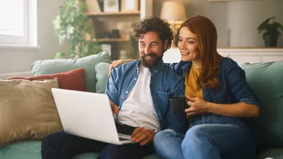 Ein Paar sitzt auf einem Sofa und schaut auf einen Laptop, während die Frau eine Tasse hält